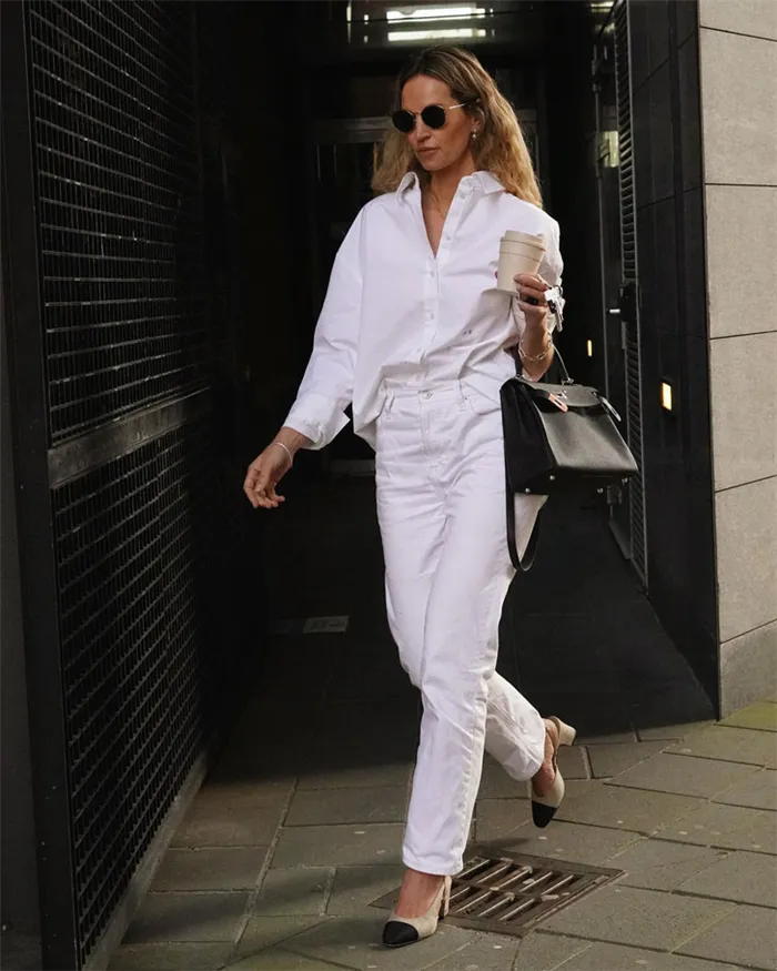 Девушка в белых прямых джинсах, безразмерной рубашке и туфлях на высоком каблуке двух цветов.