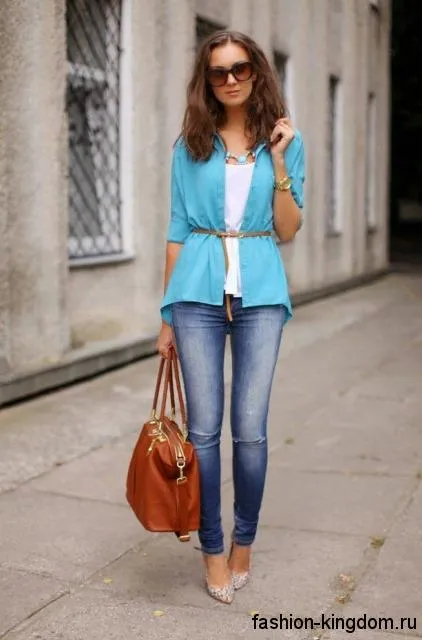 Узкие синие джинсы гармонично смотрятся с белым топом, тонкой рубашкой голубого цвета, большой рыжей сумкой и серебристыми туфлями на высоком каблуке.