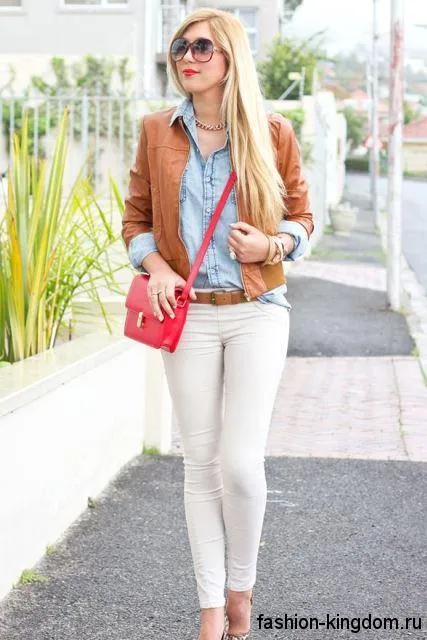 Узкие белые джинсы гармонируют с джинсовой рубашкой, короткой кожаной курткой светло-коричневого оттенка и сумочкой малинового цвета.