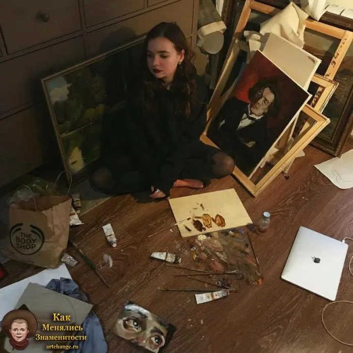 Алена Швец на фоне картин, рисунков и красок, сидит на полу
